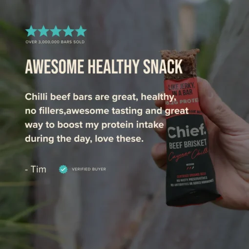 Hand holding a partially eaten Chief Beef Brisket Cayenne Chilli protein bar, labeled with 18.2g protein and certified organic beef.