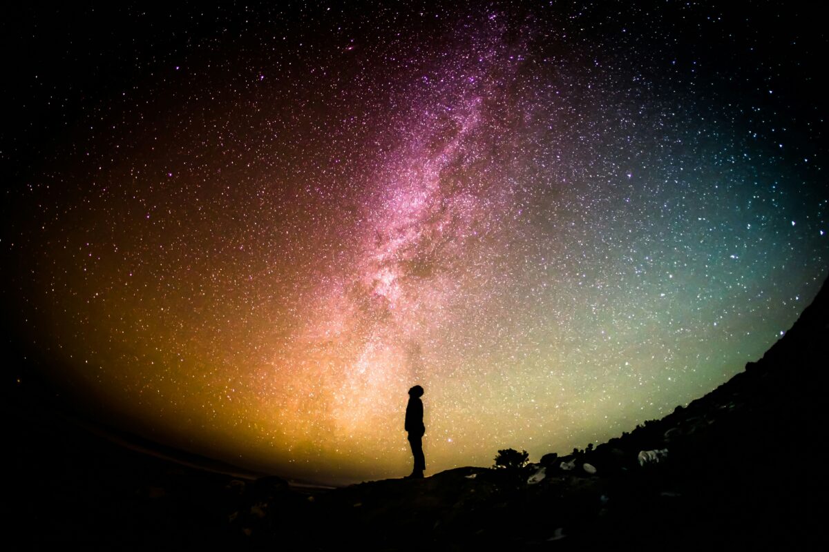 Silhouette of a person standing on a hill under a vibrant night sky filled with stars and a visible Milky Way galaxy.