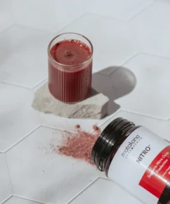 Glass of red liquid on a stone coaster next to spilled red powder and a tipped over bottle labeled Matakana Nitro.