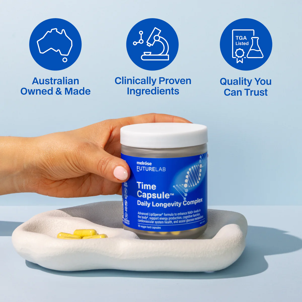 Hand holding a jar of Melrose FutureLab Time Capsule Daily Longevity Complex supplements on a white tray with yellow capsules and icons highlighting Australian owned, clinically proven ingredients, and quality assurance.